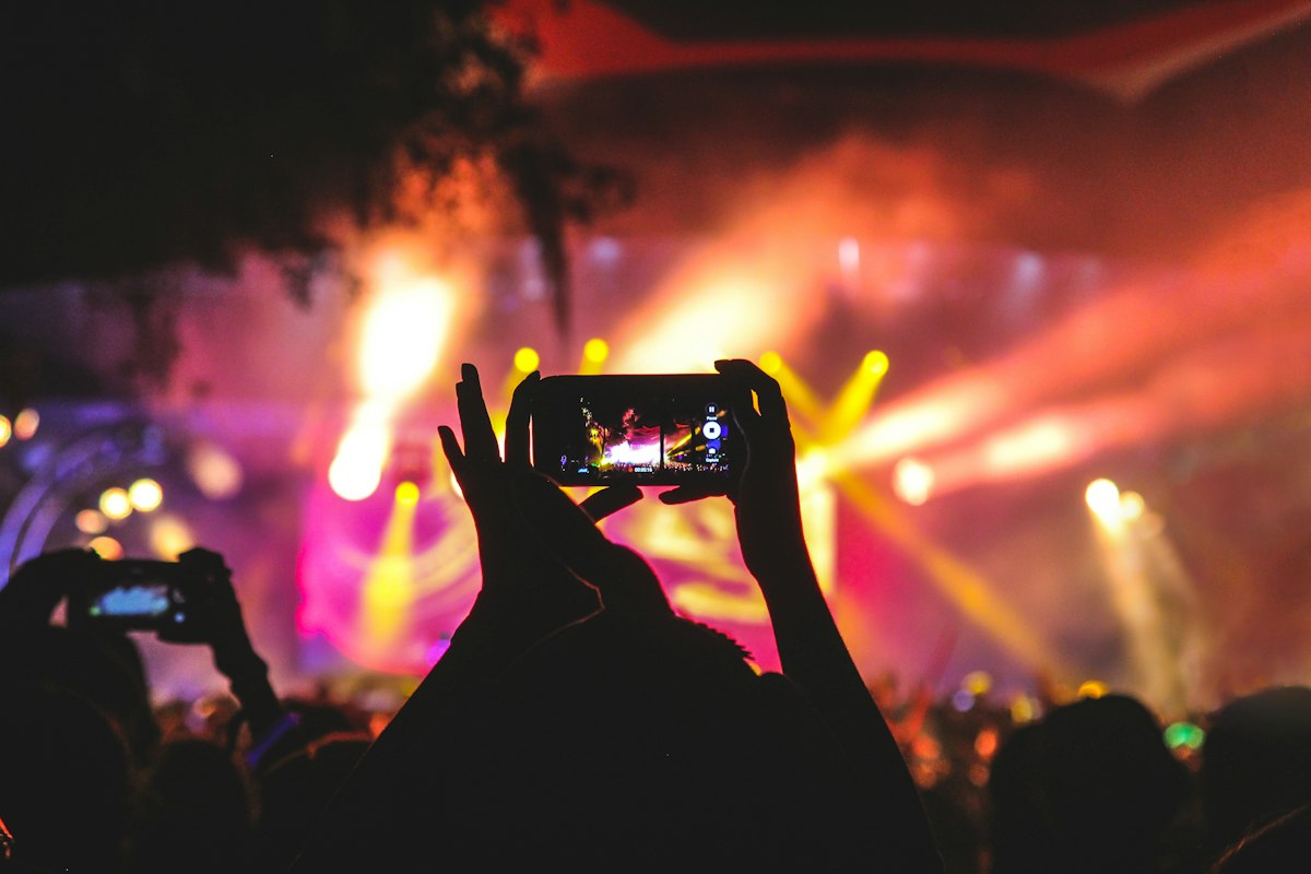 Person filming concert on phone amid lights