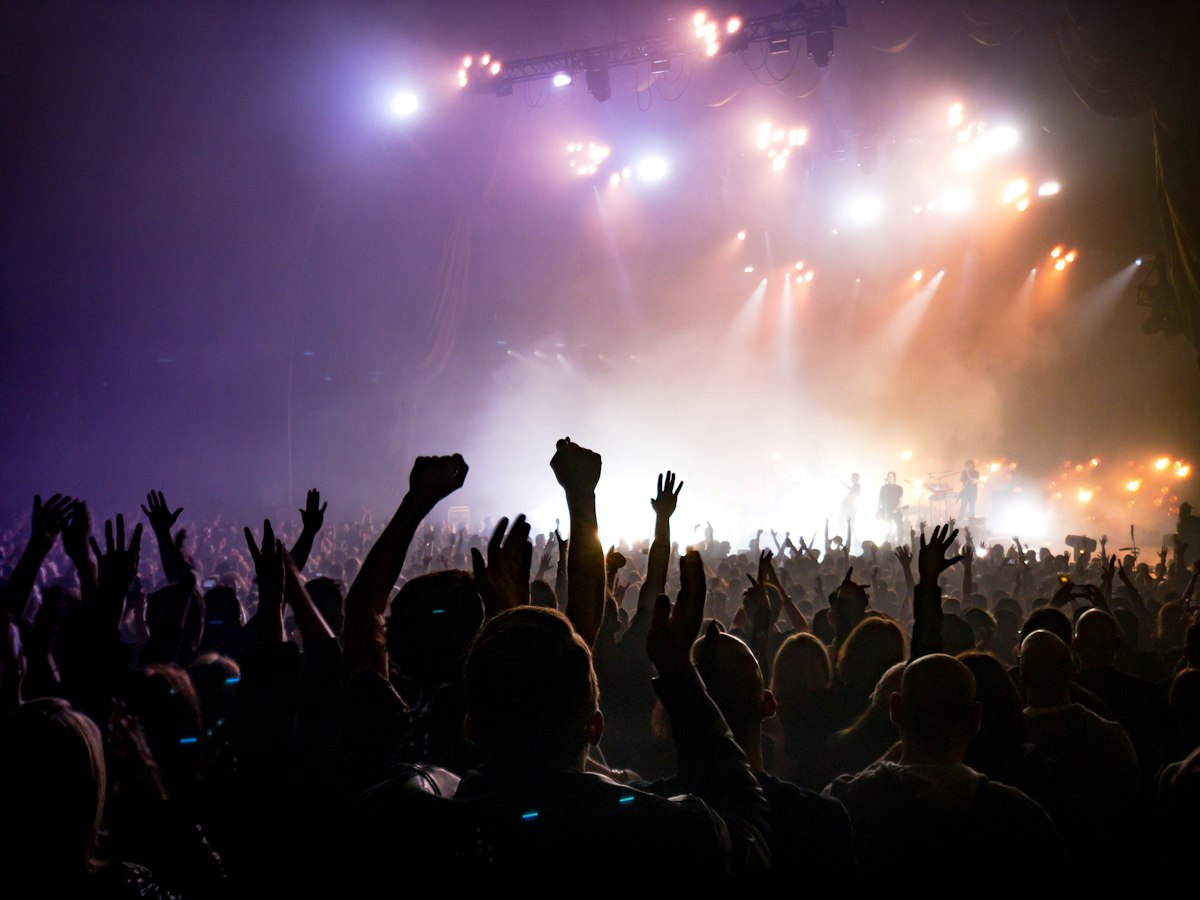 Concert crowd with raised hands facing lit stage